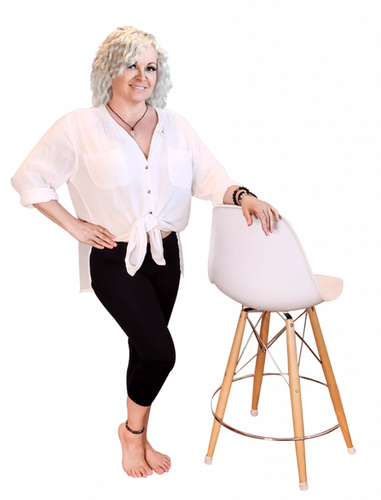 Angela Ahosaari, psychic medium and founder of Insight Intuitive in Calgary, Alberta, posing confidently with one hand on a modern chair and the other on her hip, exuding warmth and professionalism.